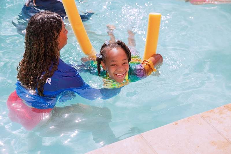 a girl swimming with a swimming instructor and a pool noodle